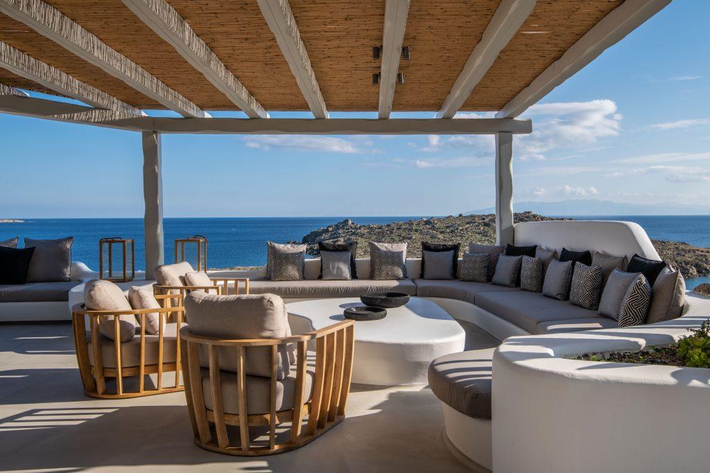 view of the blue sea of ​​Mykonos from the spacious courtyard of the villa decorated with cozy garden furniture