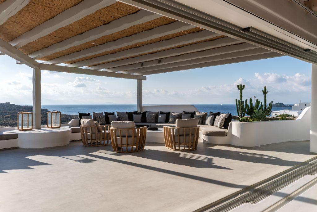 view of the blue sea of ​​Mykonos from the spacious courtyard of the villa decorated with cozy garden furniture