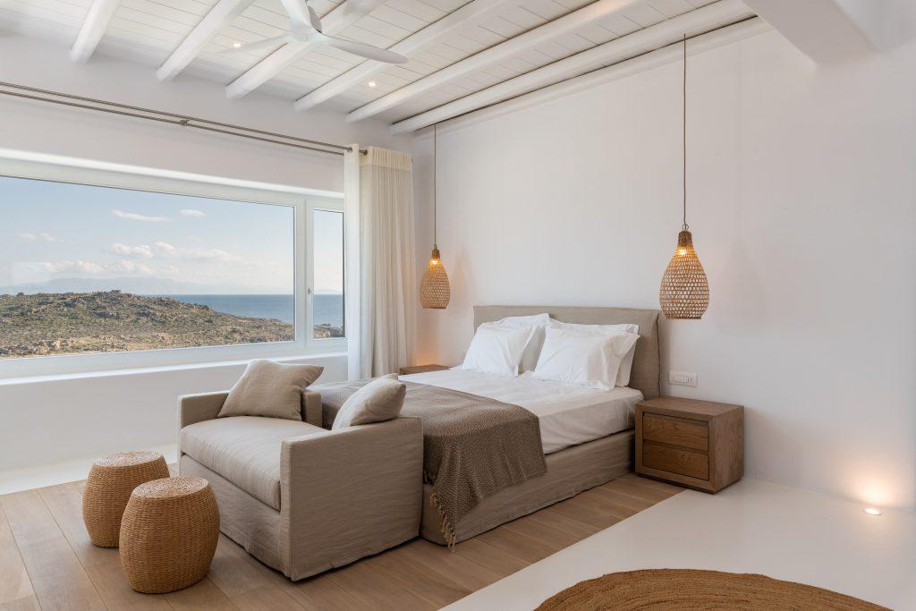 view of the light blue sea from the spacious bedroom with white walls and lots of daylight