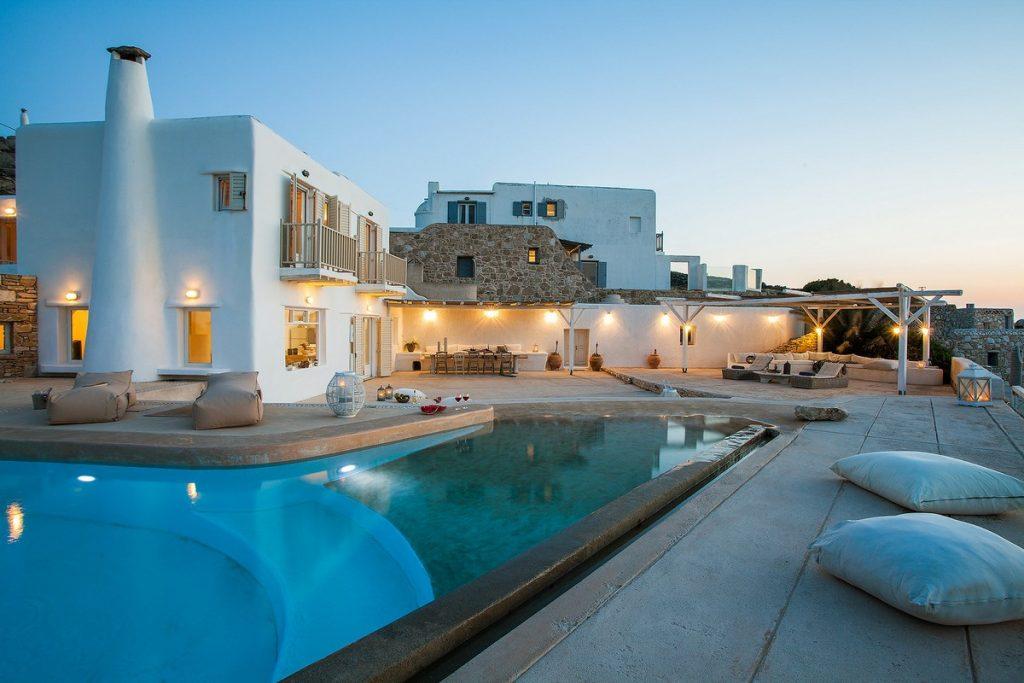 view of a white villa whose luxury is highlighted by lamps that illuminate it and a large swimming pool
